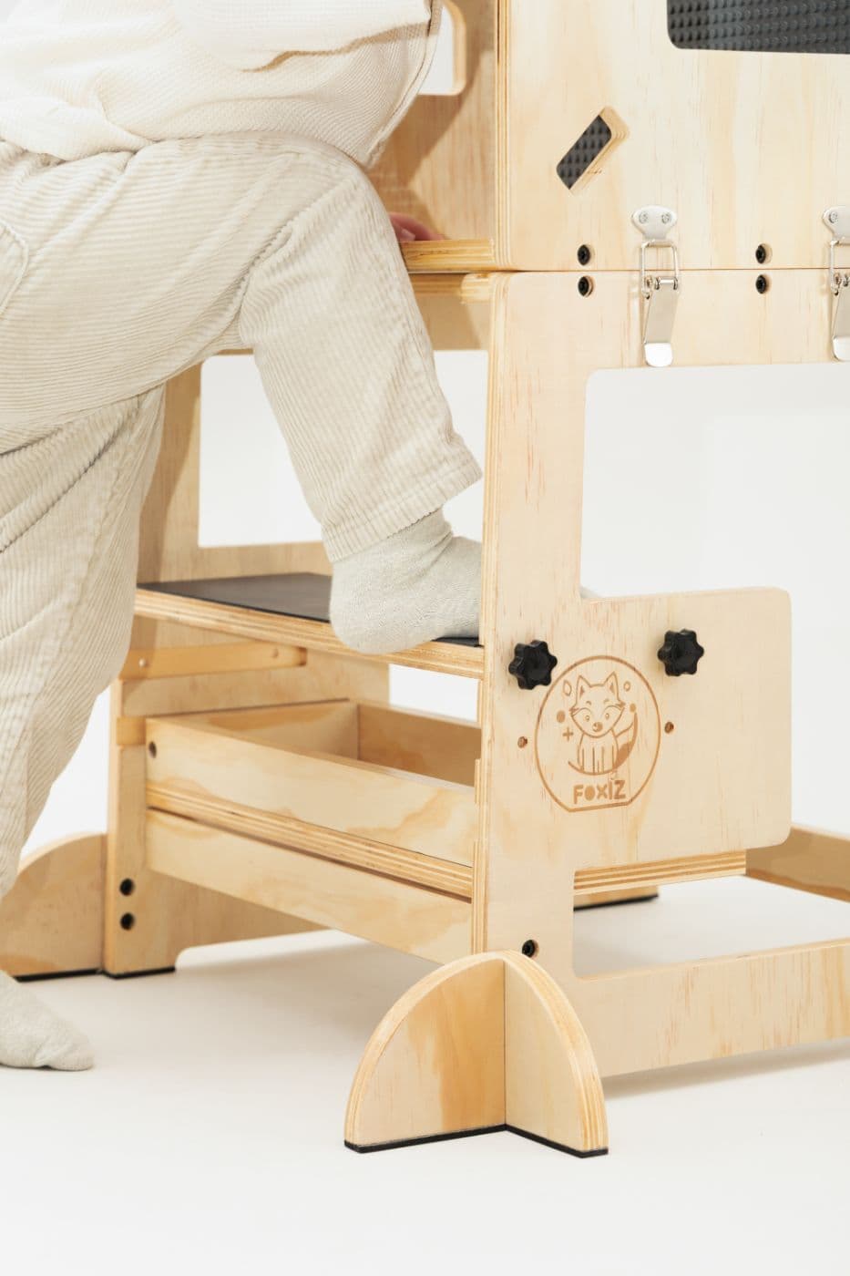 Gros plan sur le tiroir de rangement en bois glissé sous la marche de la VersaTower, qu'un enfant gravit pieds nus